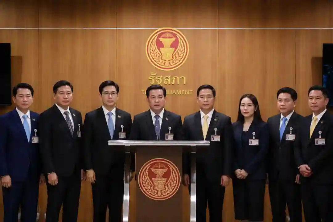 กลุ่มนักการเมืองชายและหญิงยืนแถลงข่าวหน้าพื้นหลังโลโก้รัฐสภาไทย บรรยากาศจริงจัง สุภาพ เหมาะสำหรับข่าวการเมืองและเศรษฐกิจ